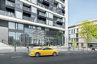 Entrance area of the Henninger Turm in Frankfurt with a yellow passing car.