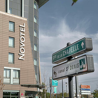 Znaki uliczne w Paryżu z fasadą hotelu Novotel w tle.