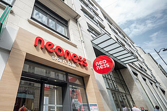 Fasada budynku mieszkalno-handlowego w Paryżu z neonowym studiem fitness na parterze i mieszkaniami powyżej.