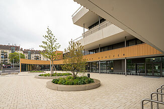 Main entrance to the Aaron Mencer Campus in Vienna with a façade made of wood, concrete and glass and surrounding terraces on several floors.