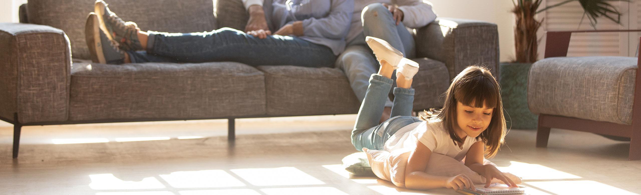 A child lies on a wooden floor and reads a book.